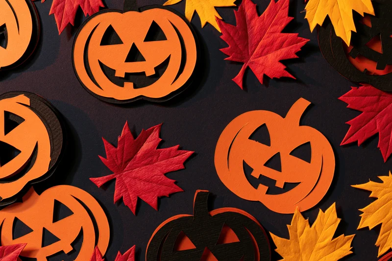 Handmade paper jack-o-lanterns and autumn leaves arranged in a flat lay on dark background