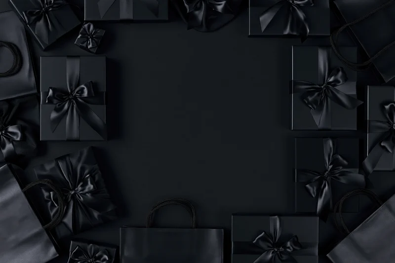 Black gift boxes with satin ribbon bows arranged in a frame around copyspace