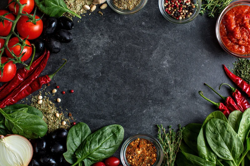 Pizza ingredients arranged around edges of dark countertop with central copyspace