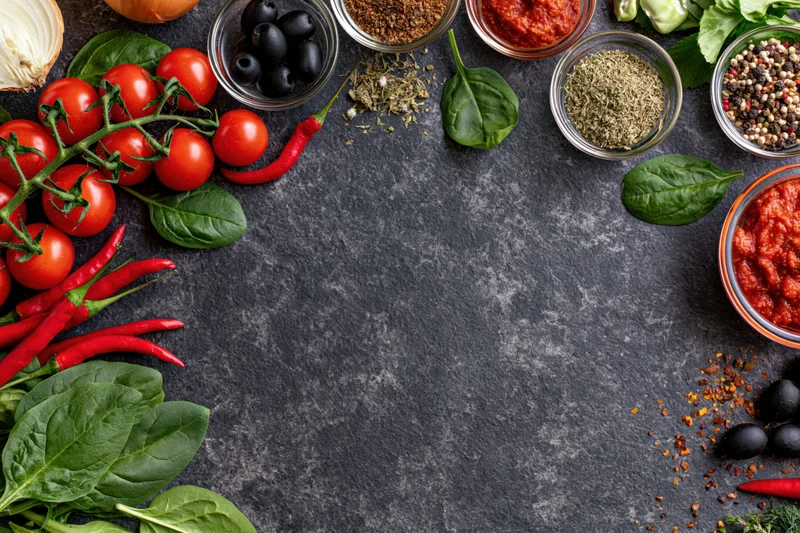 Pizza ingredients arranged around the edges of a dark stone countertop with copyspace in center
