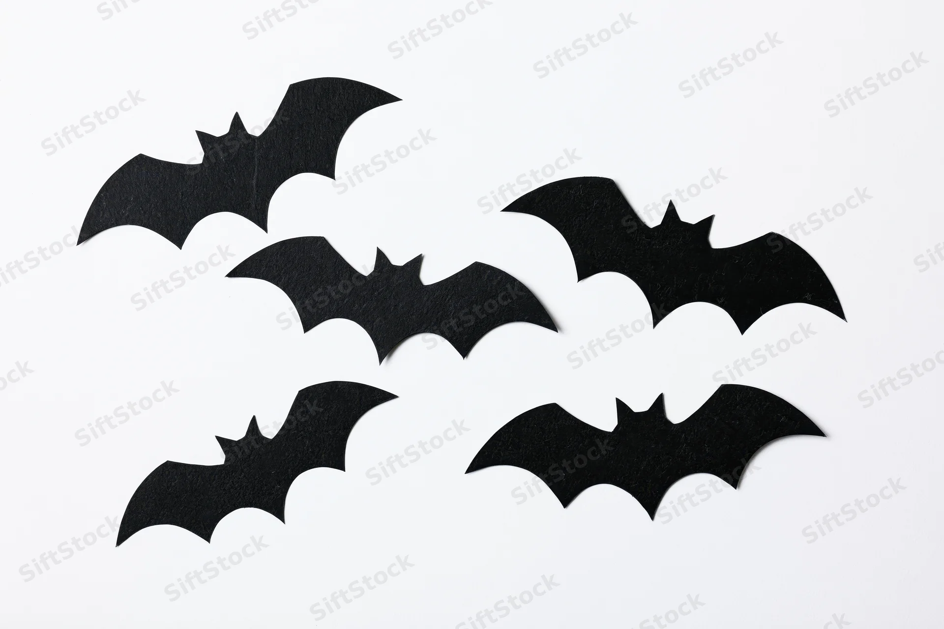 Black paper bat cutouts arranged in a loose flying formation on white background