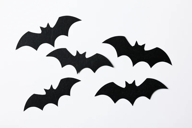 Black paper bat cutouts arranged in a loose flying formation on white background