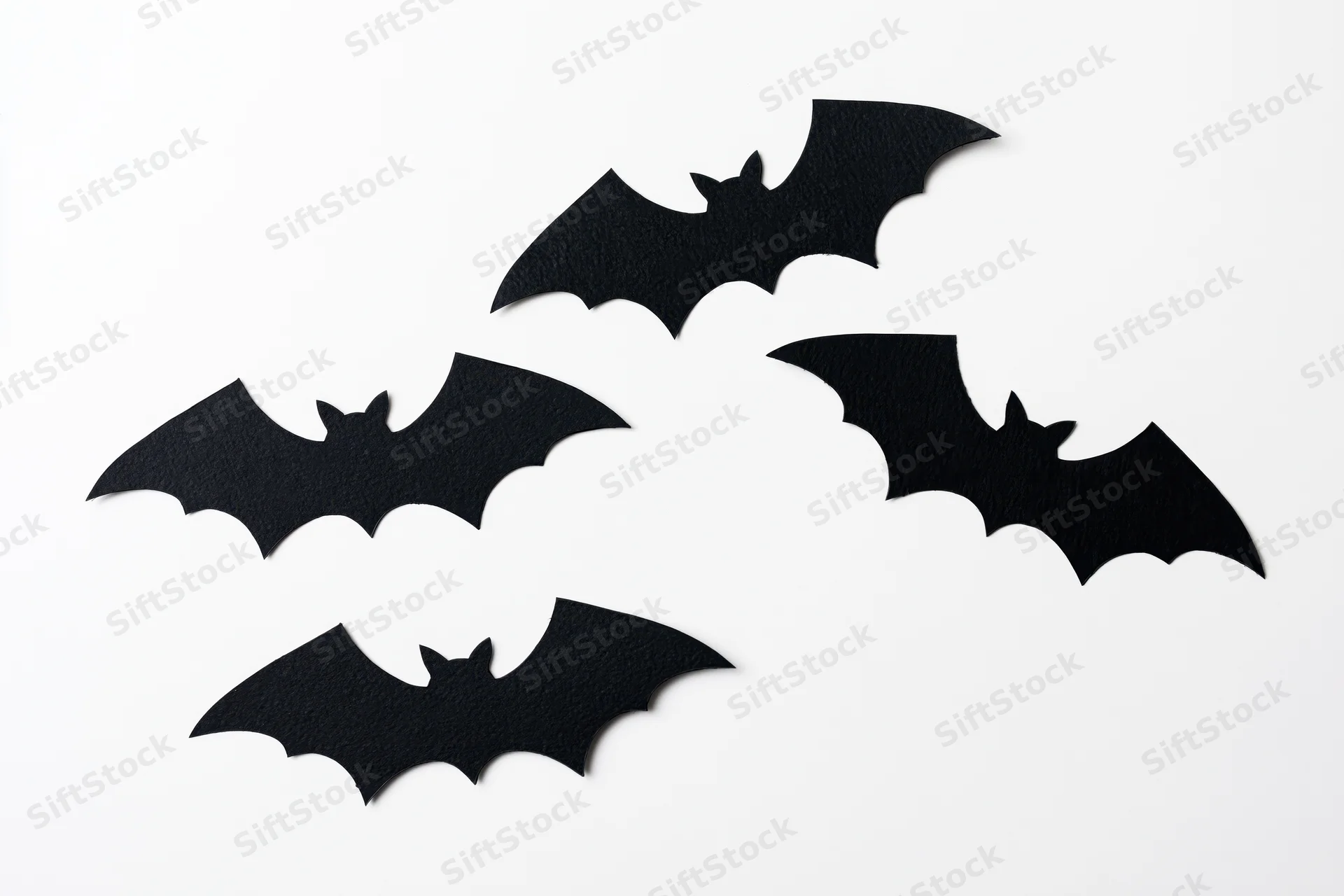 Four black paper bat cutouts arranged in a loose flying formation on white background