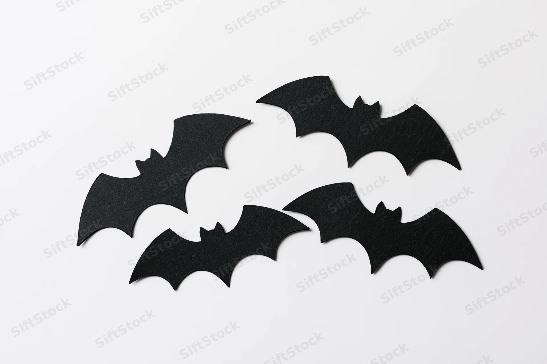 Four black paper bat cutouts arranged in a loose flying formation on white background