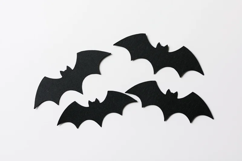 Four black paper bat cutouts arranged in a loose flying formation on white background