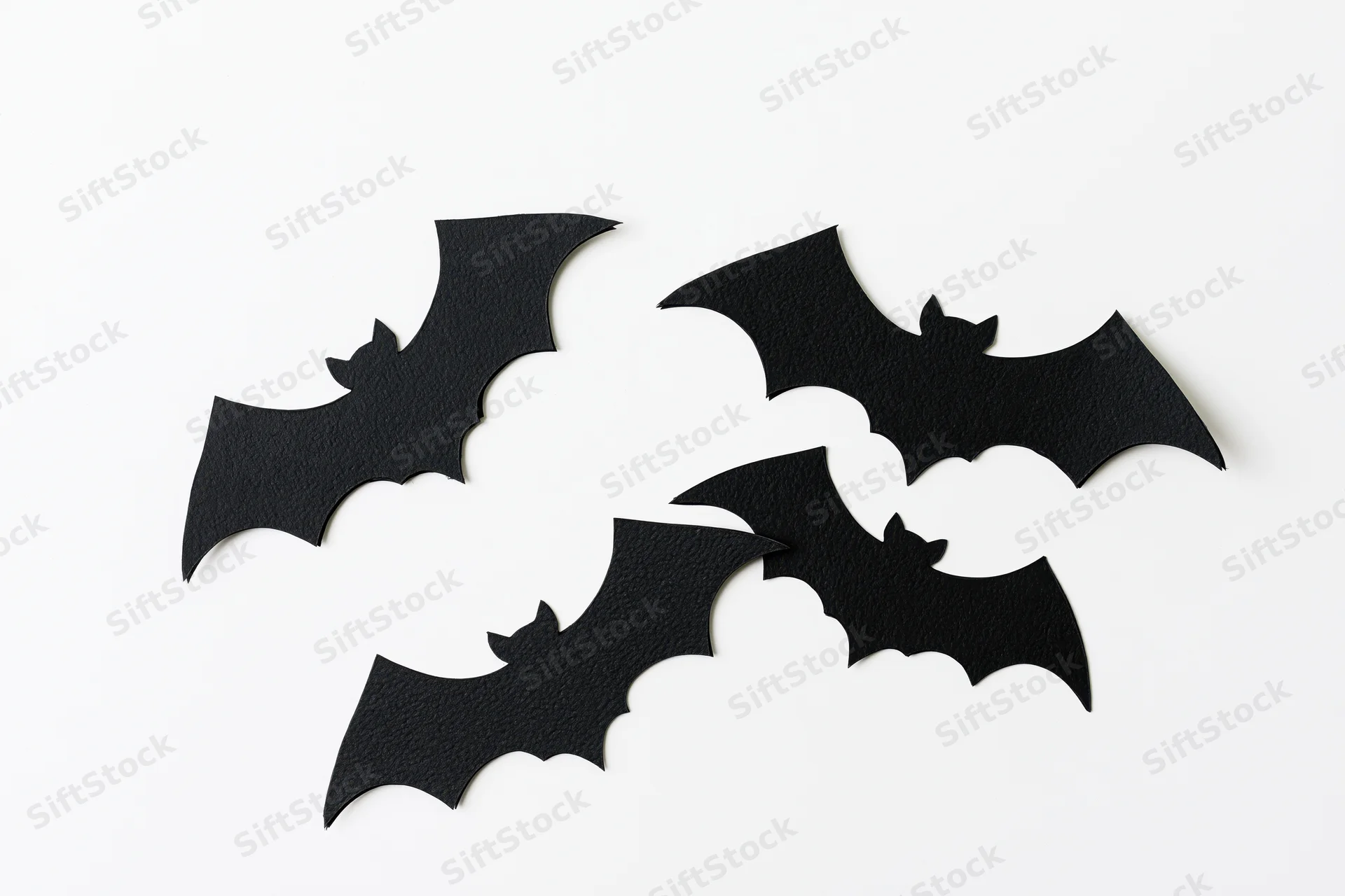 Four black paper bat cutouts arranged in a loose flying formation on white background