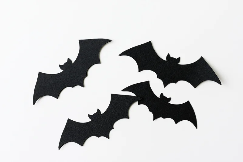 Four black paper bat cutouts arranged in a loose flying formation on white background