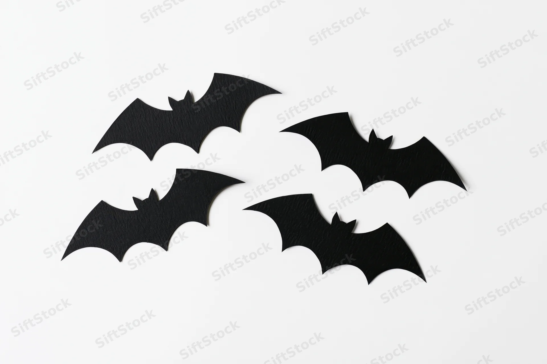 Four black paper bat cutouts arranged in a loose flying formation on white background