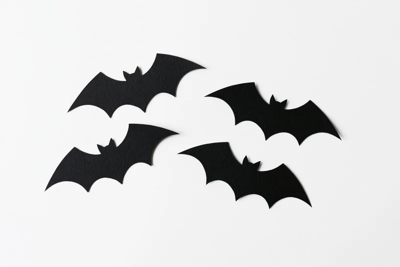 Four black paper bat cutouts arranged in a loose flying formation on white background