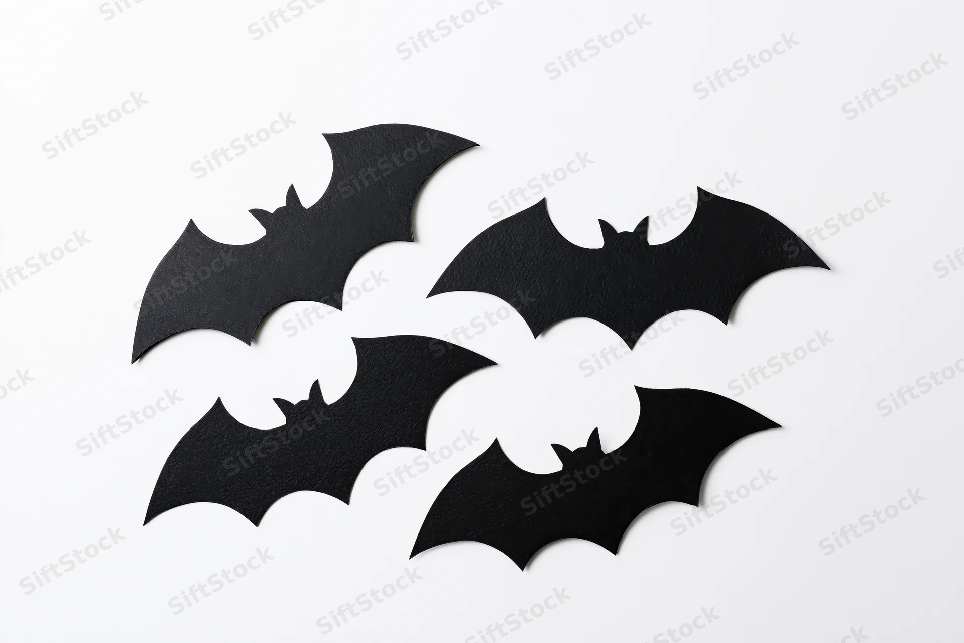 Four black paper bat cutouts arranged in a loose flying formation on white background