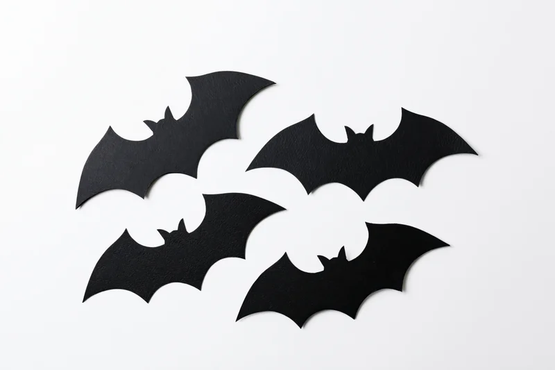 Four black paper bat cutouts arranged in a loose flying formation on white background