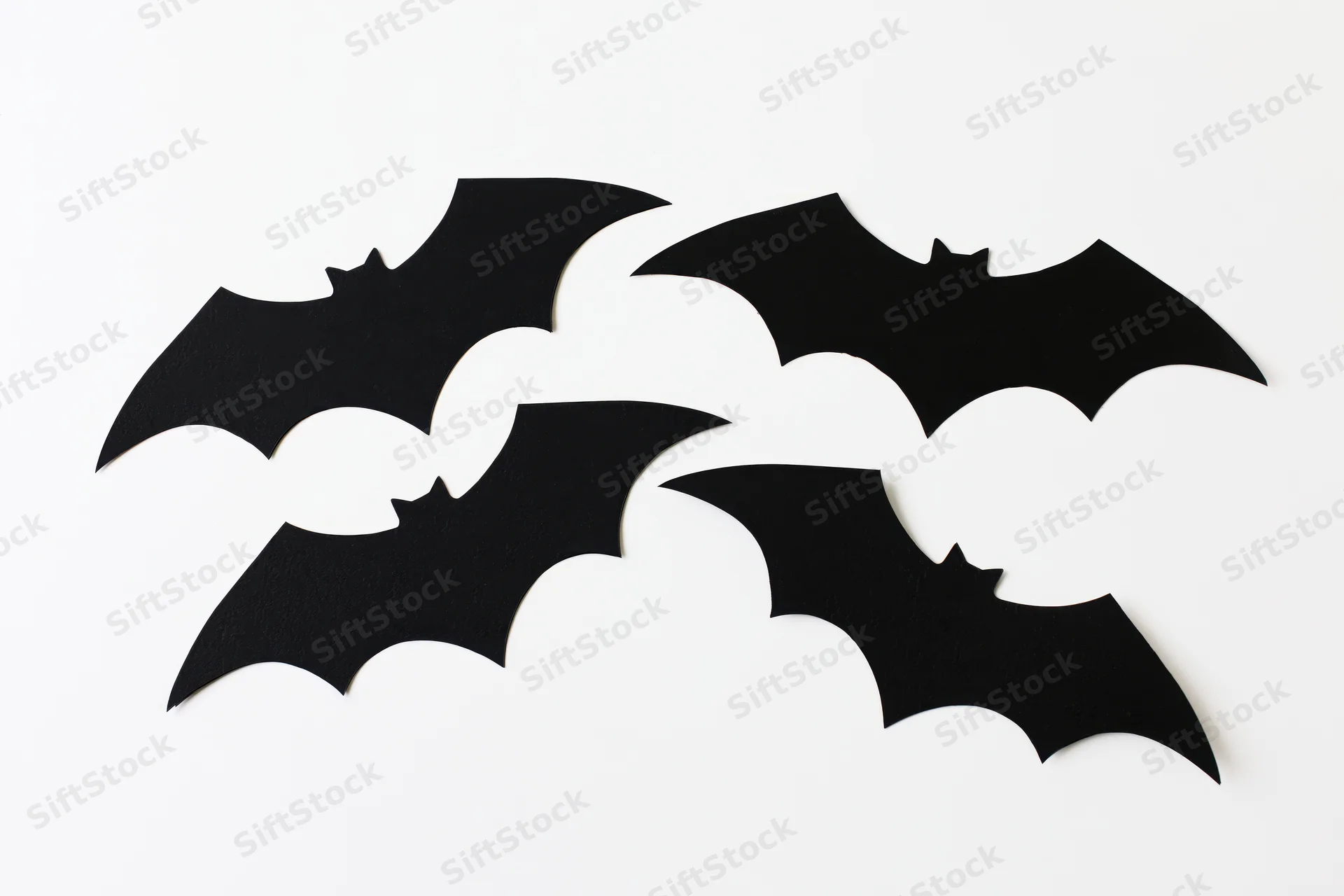 Four black paper bat cutouts arranged in a loose flying formation on white background
