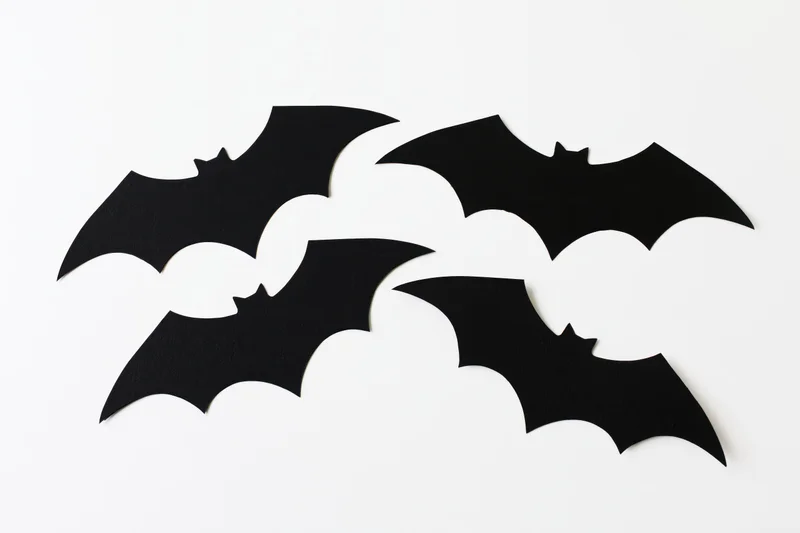 Four black paper bat cutouts arranged in a loose flying formation on white background