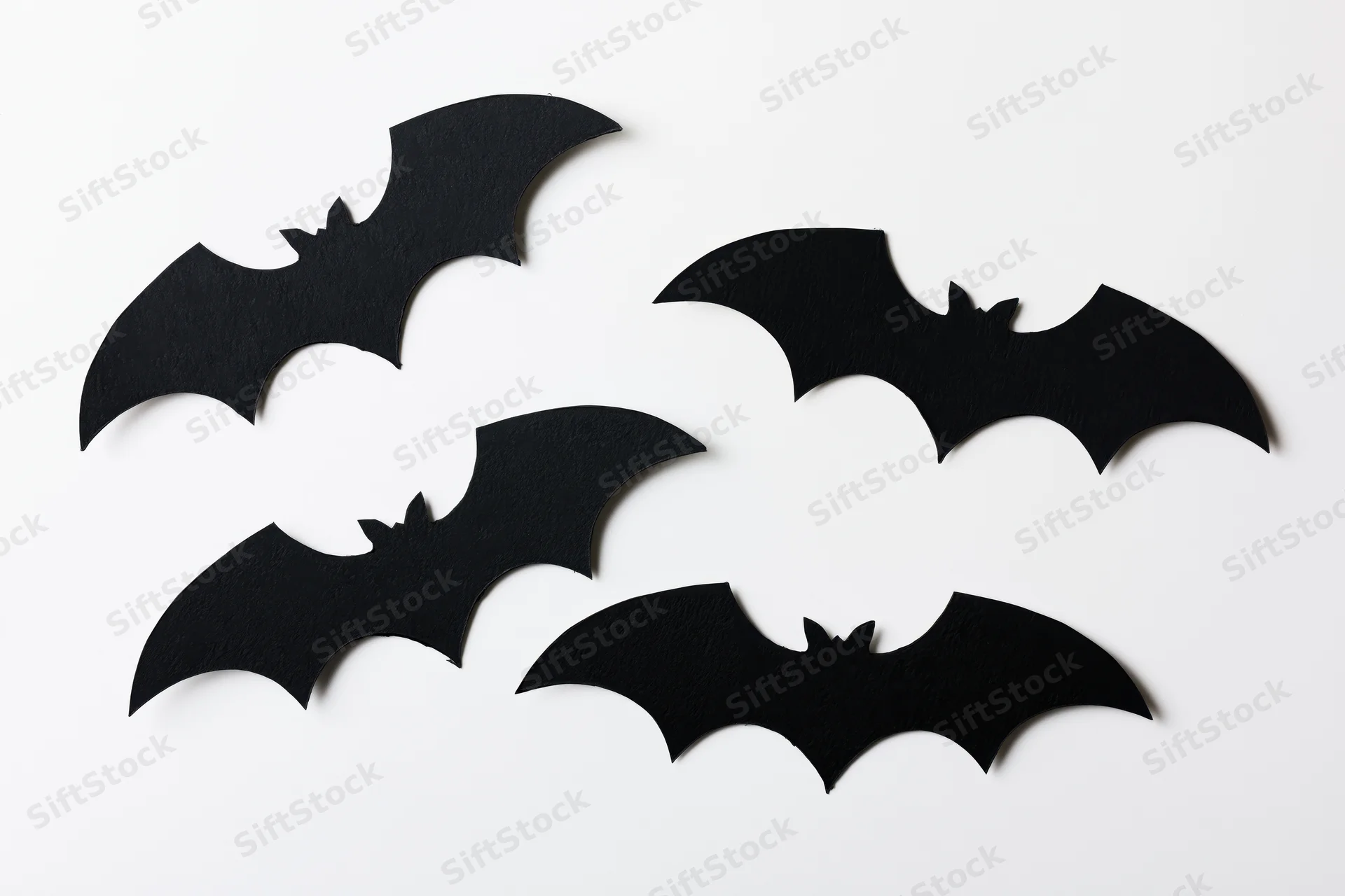 Four black paper bat cutouts arranged in a loose flying formation on white background