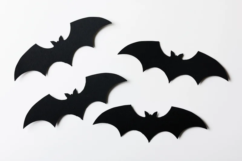 Four black paper bat cutouts arranged in a loose flying formation on white background