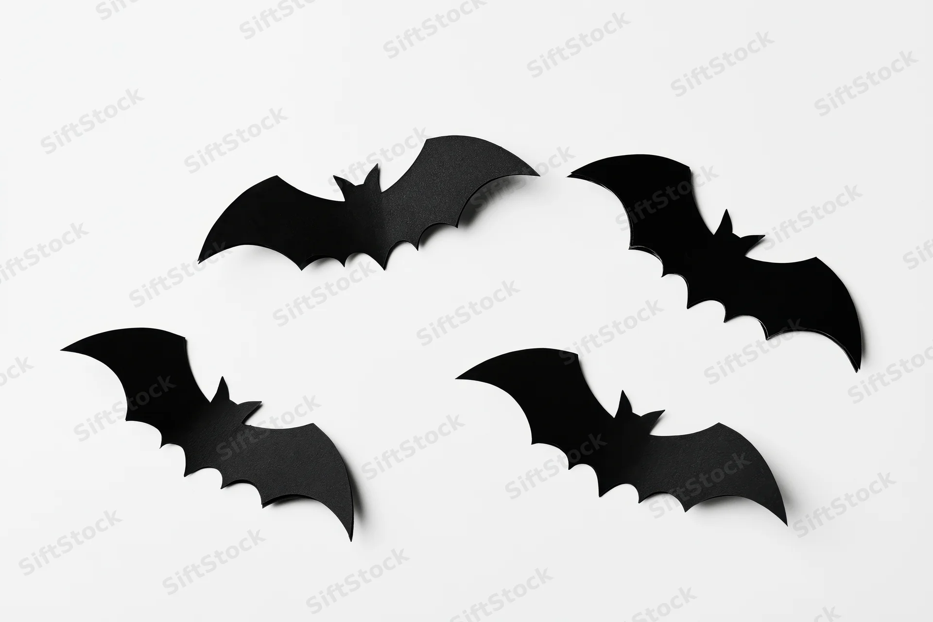 Four black paper bat cutouts arranged in a loose flying formation on white background