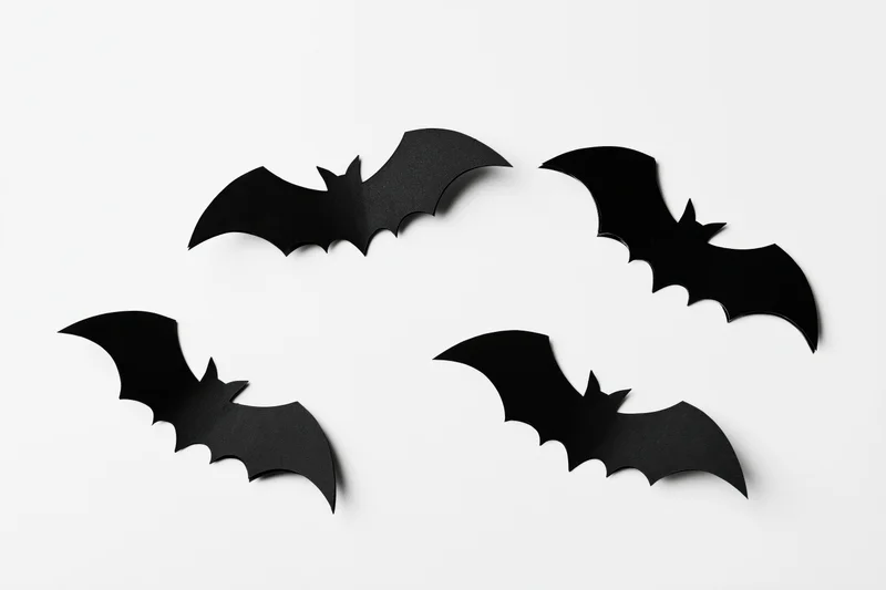 Four black paper bat cutouts arranged in a loose flying formation on white background