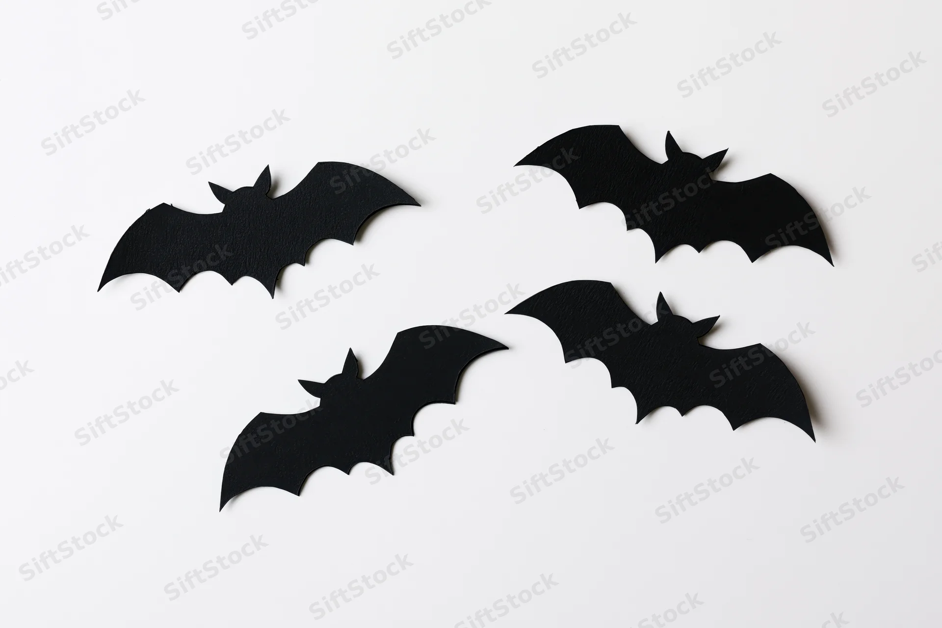 Four black paper bat cutouts arranged in a loose flying formation on a white surface