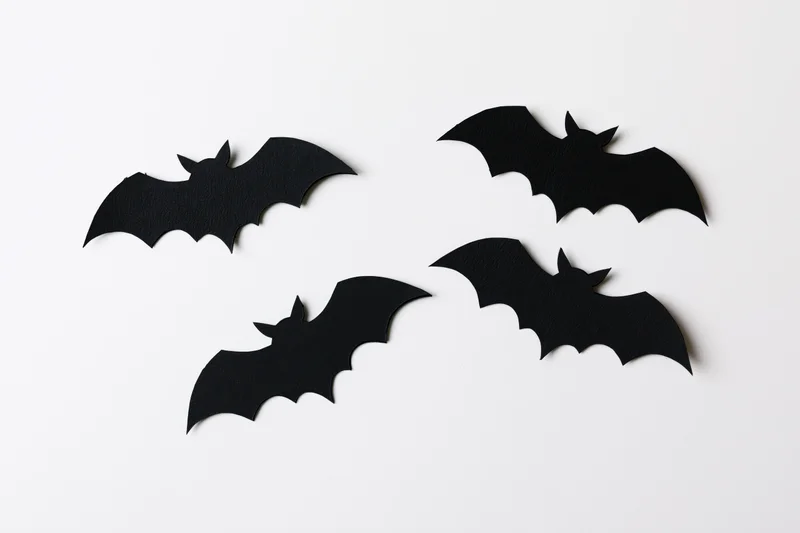 Four black paper bat cutouts arranged in a loose flying formation on a white surface