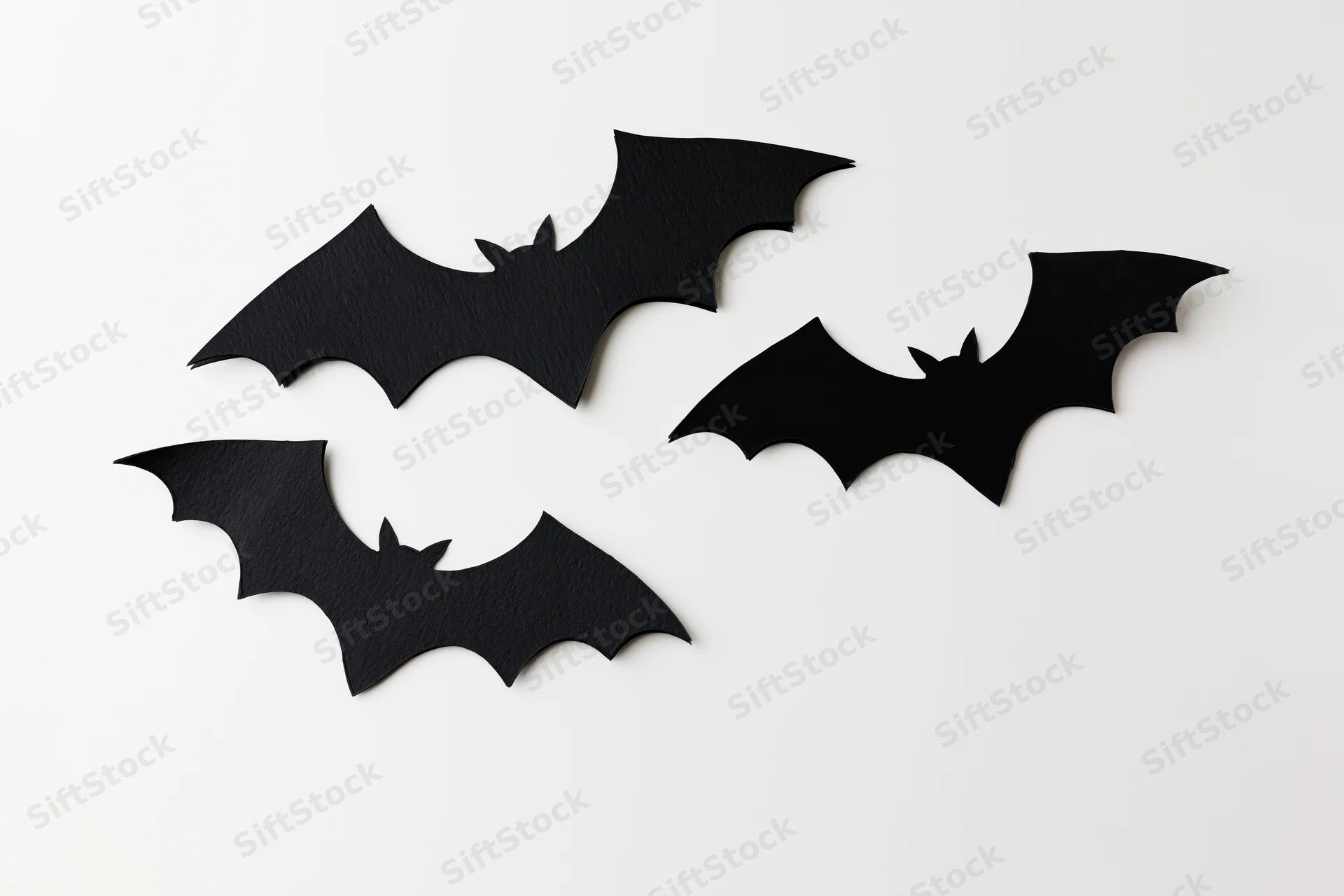 Three black paper bat cutouts arranged in a loose flying formation on a white surface