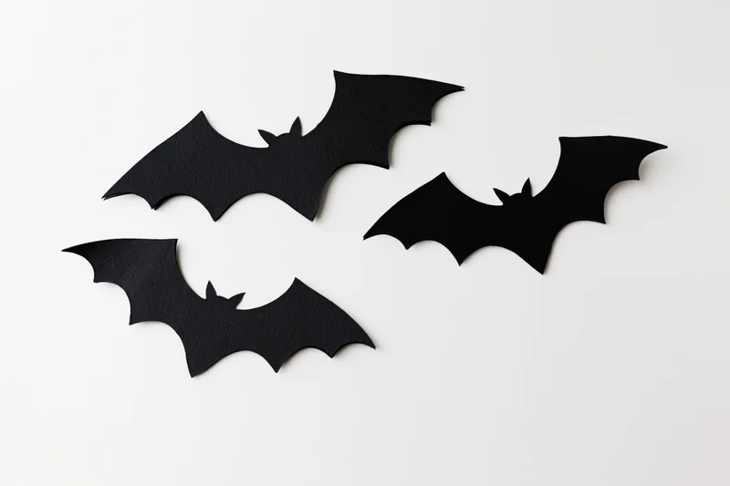 Three black paper bat cutouts arranged in a loose flying formation on a white surface