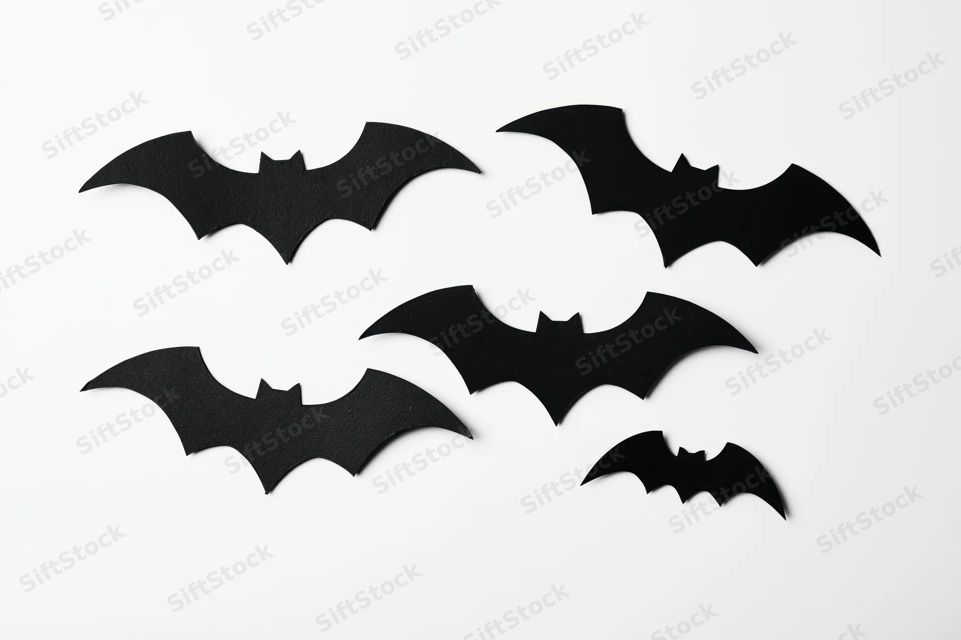 Black paper bat cutouts arranged in a loose flying formation on white background