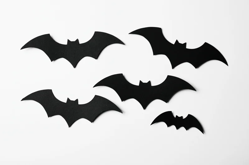 Black paper bat cutouts arranged in a loose flying formation on white background