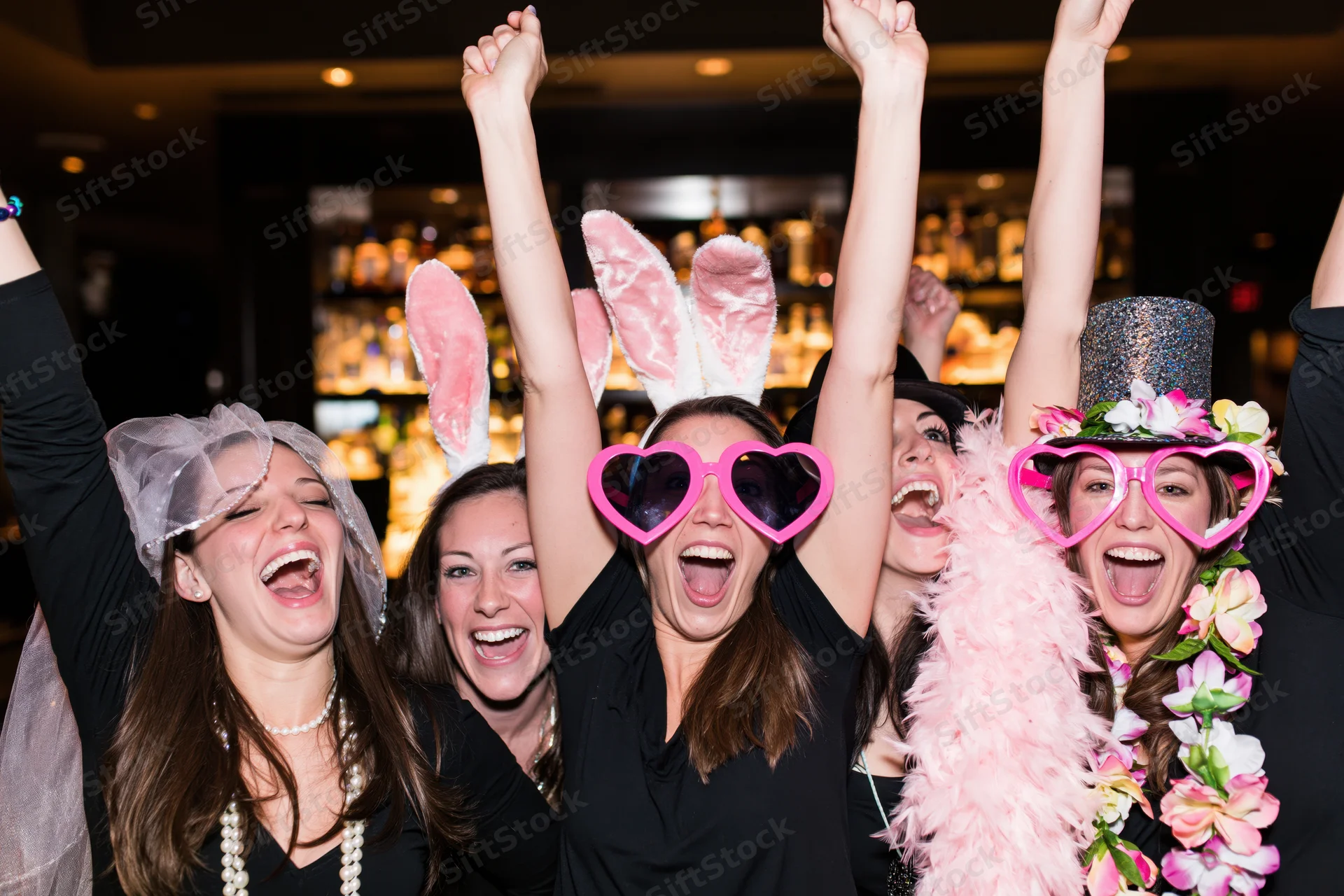 Four women celebrating a bachelorette party in a nightclub with festive accessories and raised arms