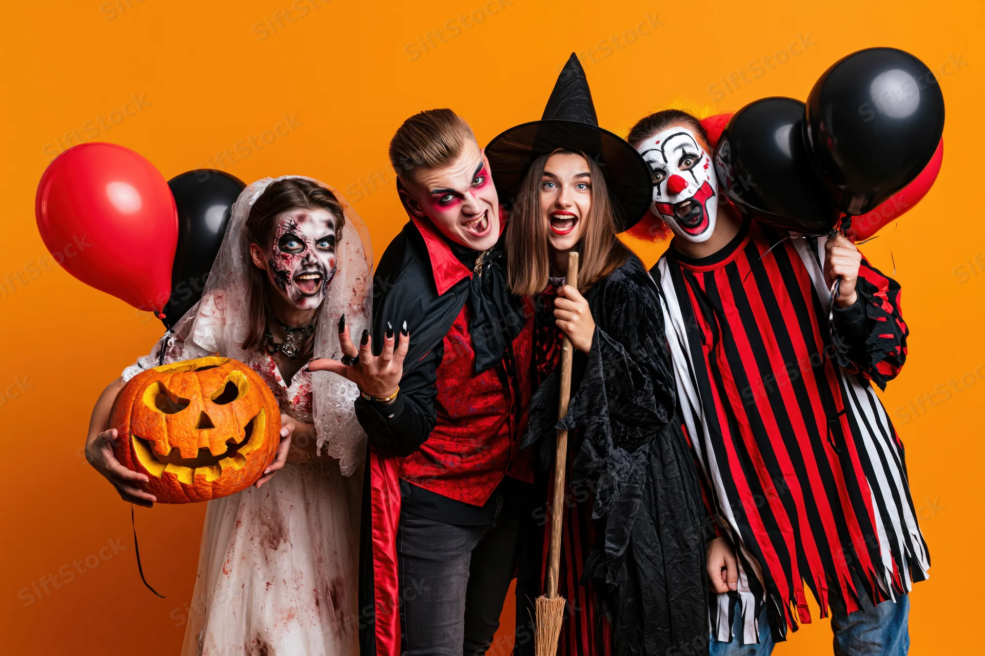 Four young adults in halloween costumes posing together in studio with pumpkins and balloons