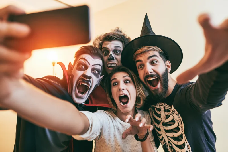 Four young adults in halloween costumes taking a group selfie indoors