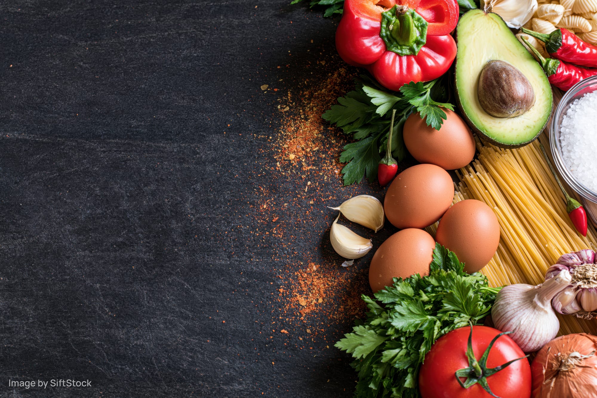 Fresh cooking ingredients arranged along the right edge of a dark slate surface