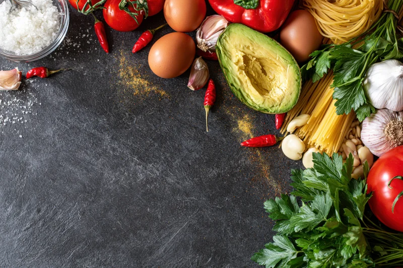 Fresh cooking ingredients arranged along the right edge of a dark slate countertop with copyspace on the left