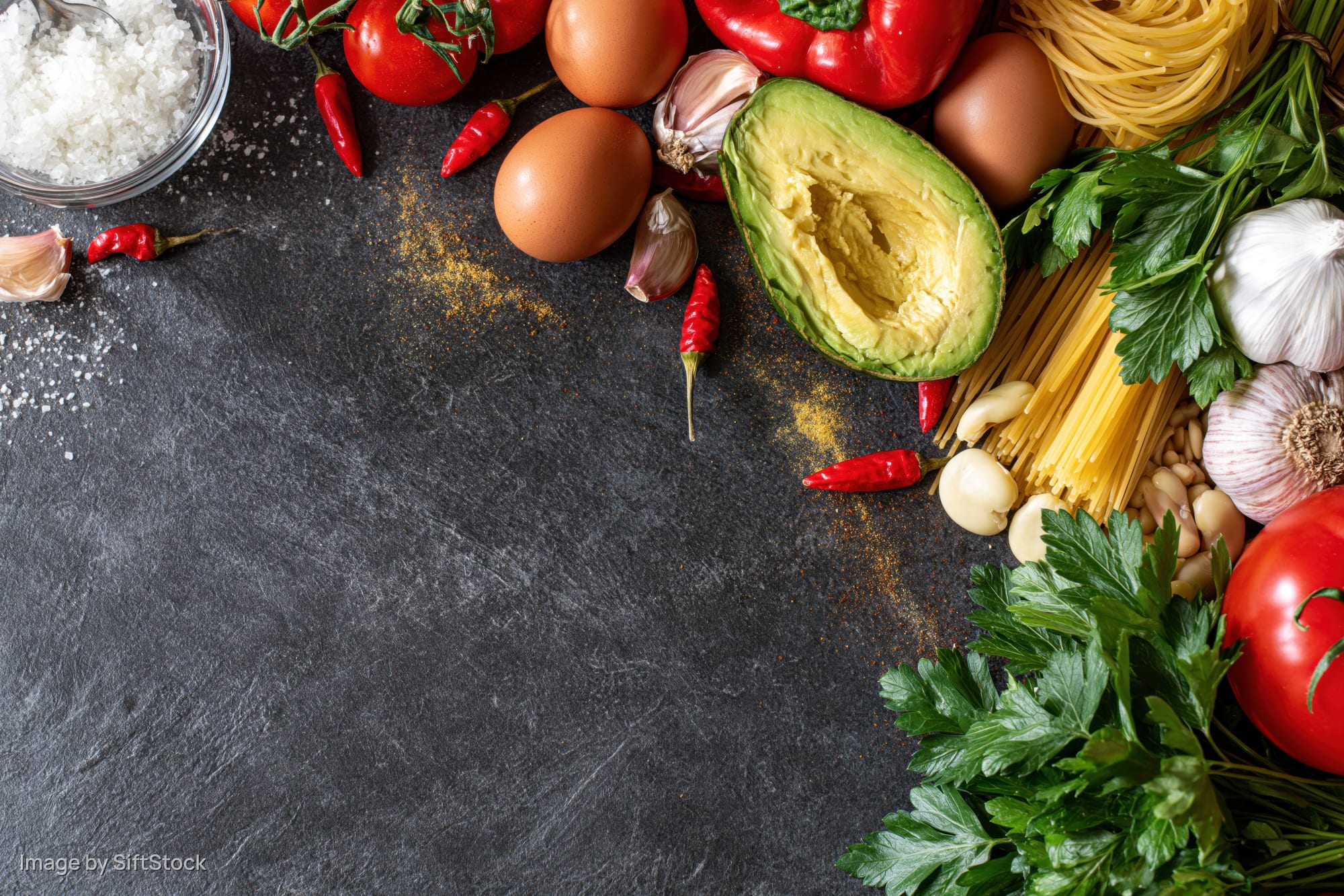 Fresh cooking ingredients arranged along the right edge of a dark slate countertop with copyspace on the left