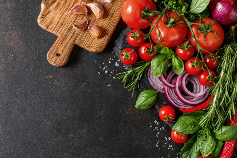 Fresh vegetables and herbs arranged along the right edge of a dark surface with copyspace on the left