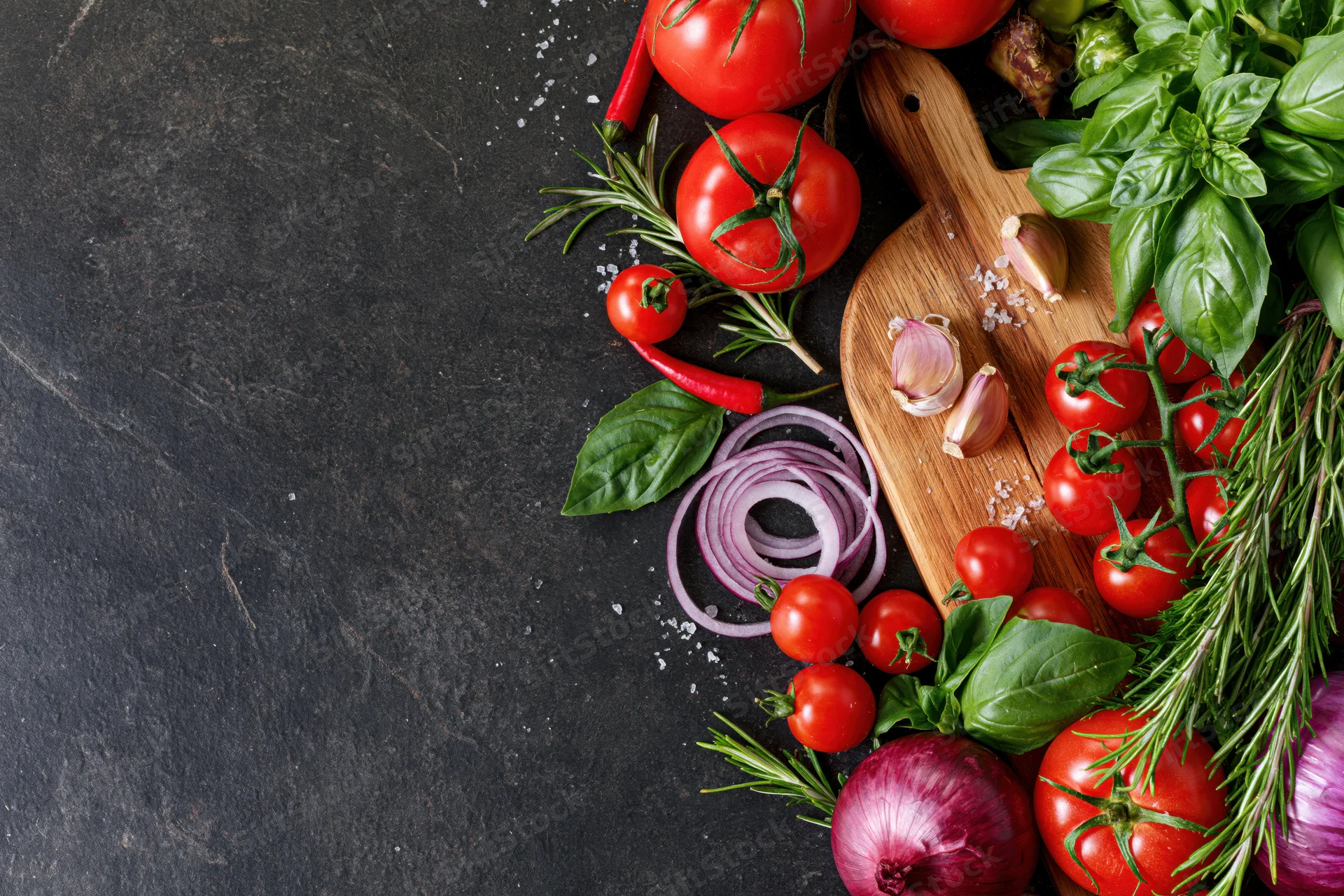 Fresh vegetables and herbs arranged along the right edge of a dark slate surface with copyspace on the left