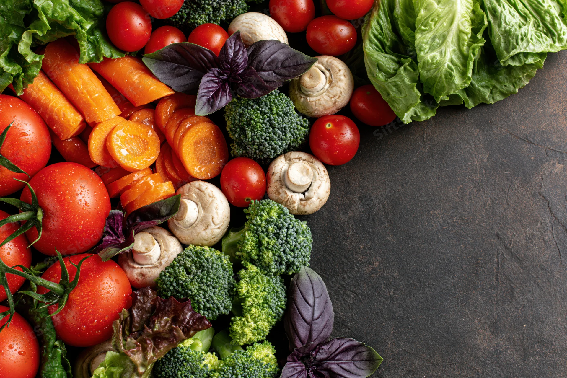 Fresh vegetables arranged along the left and top edge on dark slate surface