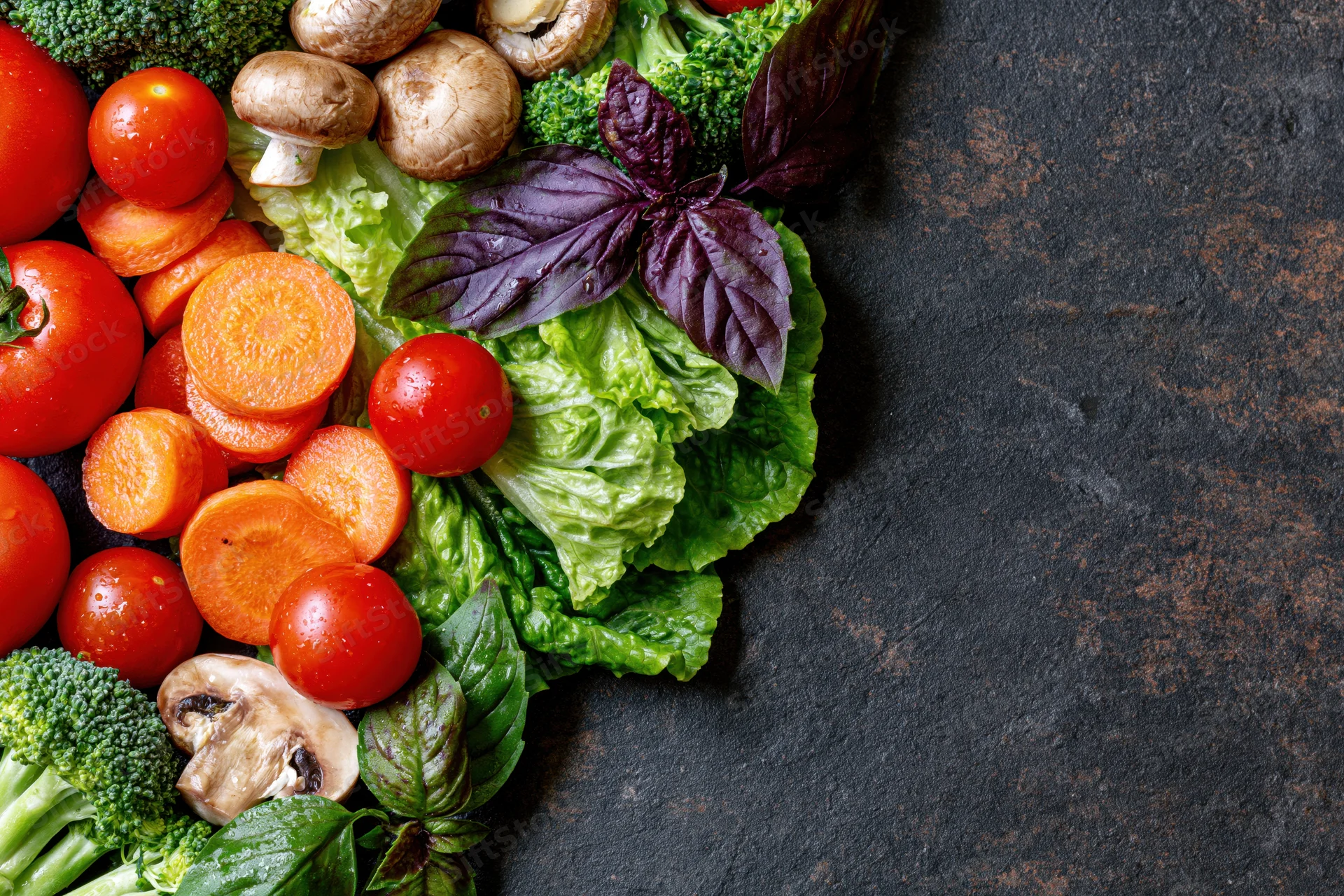 Fresh vegetables arranged along the left and top edge on a dark stone surface