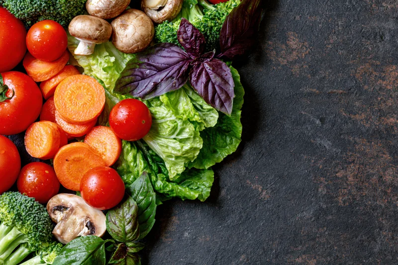 Fresh vegetables arranged along the left and top edge on a dark stone surface