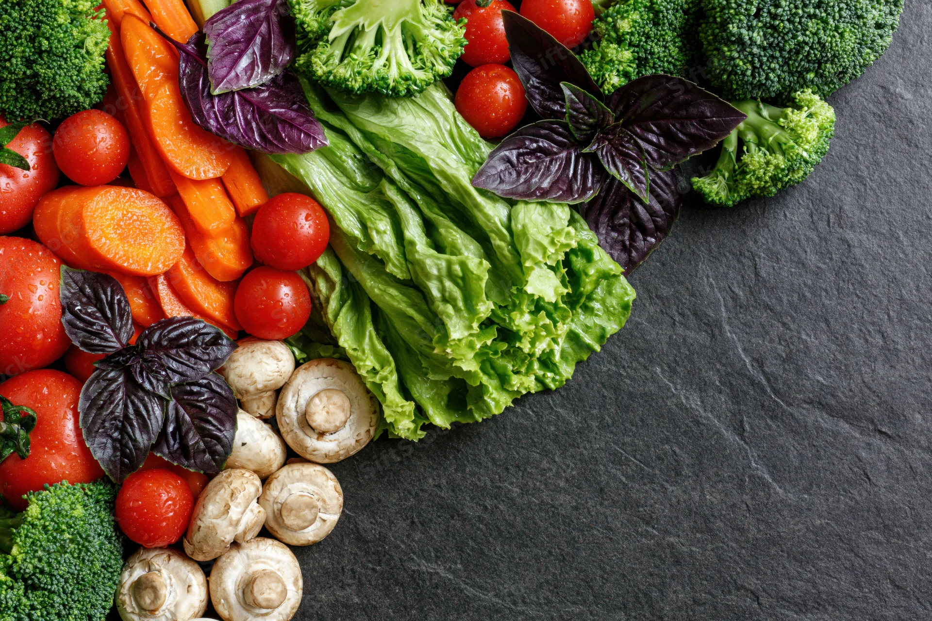 Fresh vegetables arranged along the left and top edge on a dark slate surface