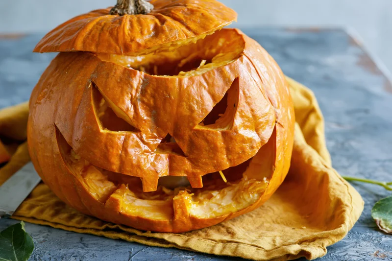 Carved pumpkin with jagged triangular eyes and wide grin resting on a yellow cloth on a stone surface