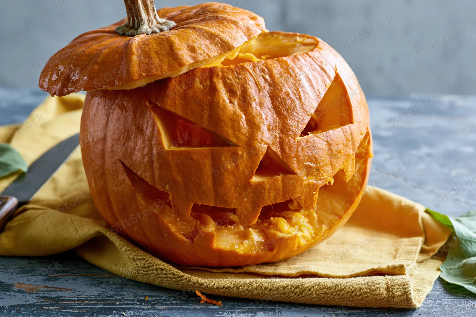 Carved pumpkin with jagged triangular eyes and mouth on a yellow cloth on a dark wooden table