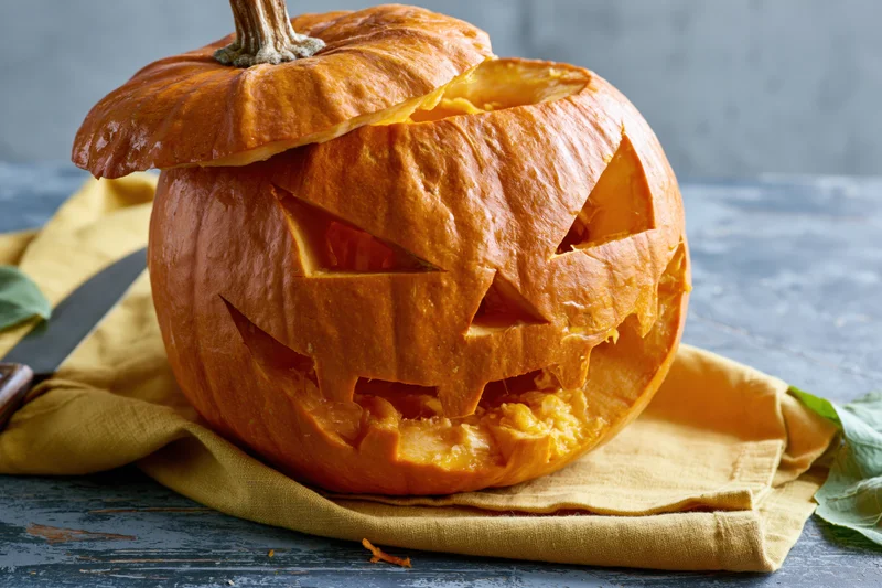 Carved pumpkin with jagged triangular eyes and mouth on a yellow cloth on a dark wooden table