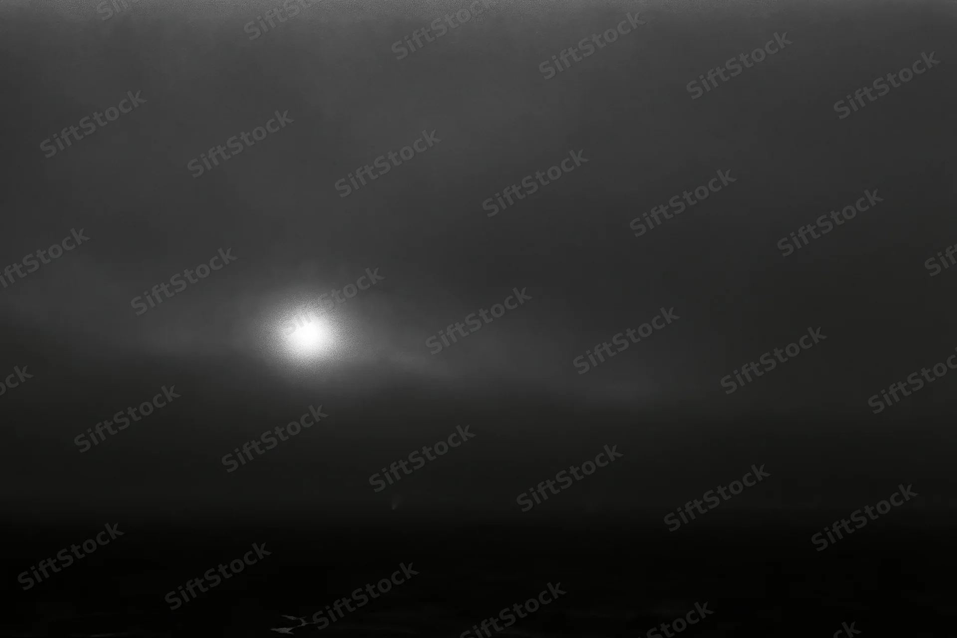 Full moon glowing through thick storm clouds over dark water