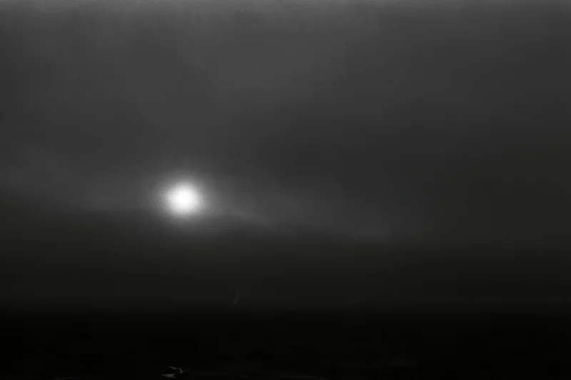 Full moon glowing through thick storm clouds over dark water