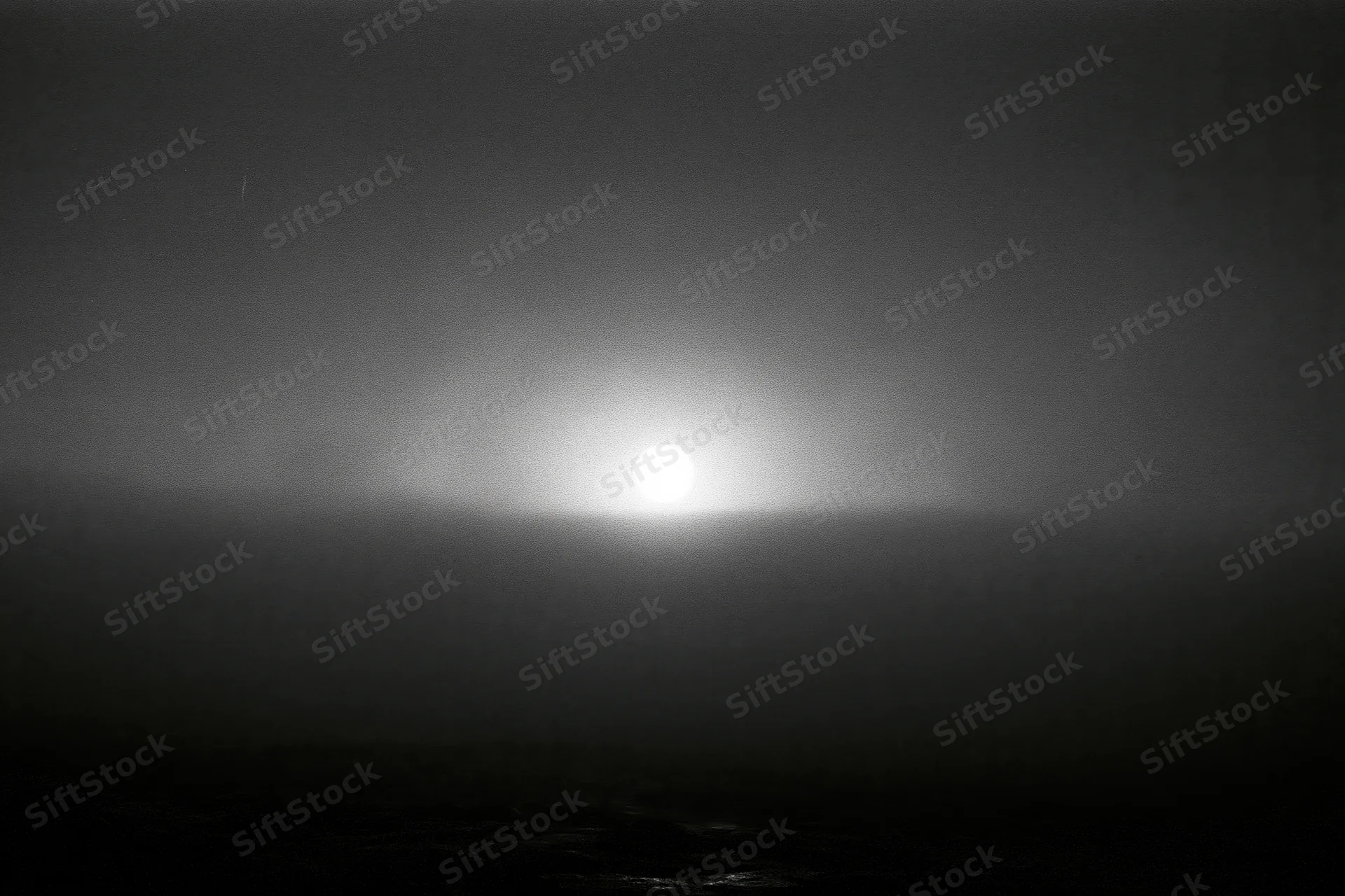 Full moon glowing through thick storm clouds over dark rocky shore