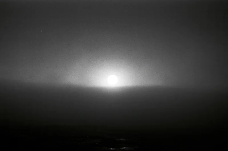Full moon glowing through thick storm clouds over dark rocky shore