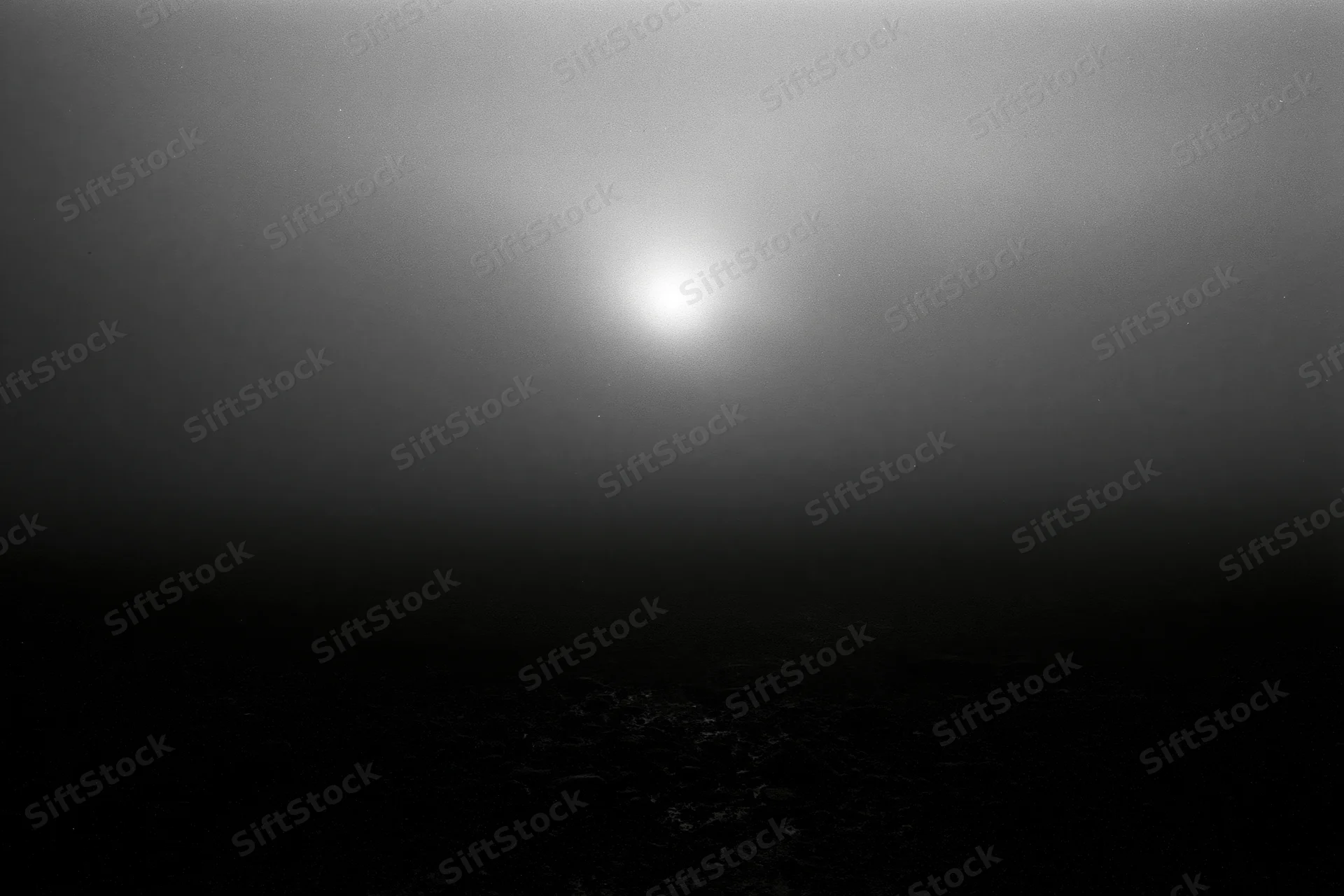 Full moon glowing through thick storm clouds over dark rocky surface