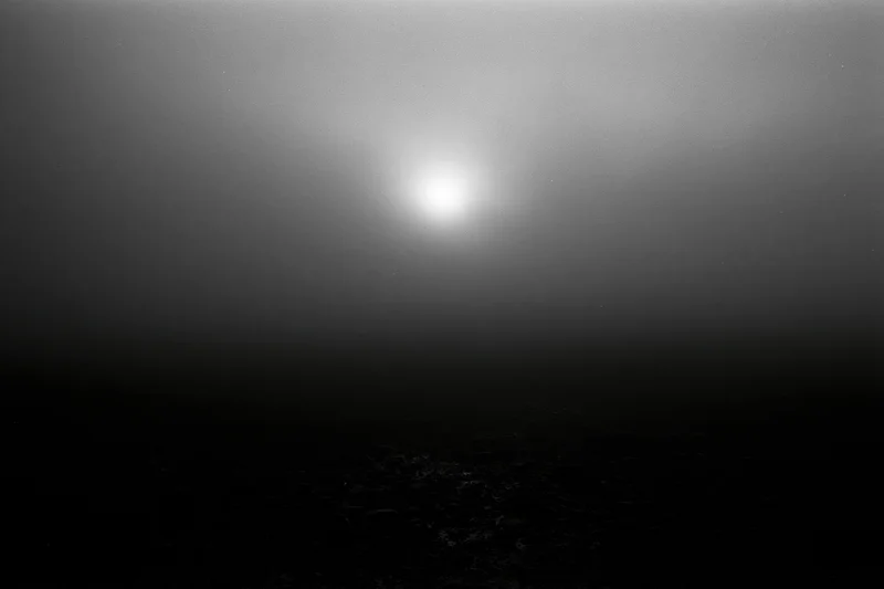 Full moon glowing through thick storm clouds over dark rocky surface