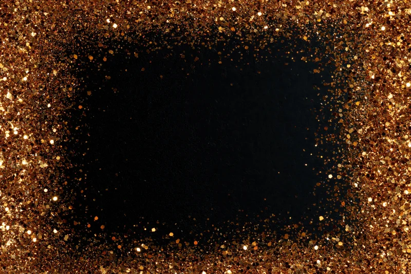 Gold glitter particles forming a circular frame around a dark center, creating a festive border with copyspace in the middle