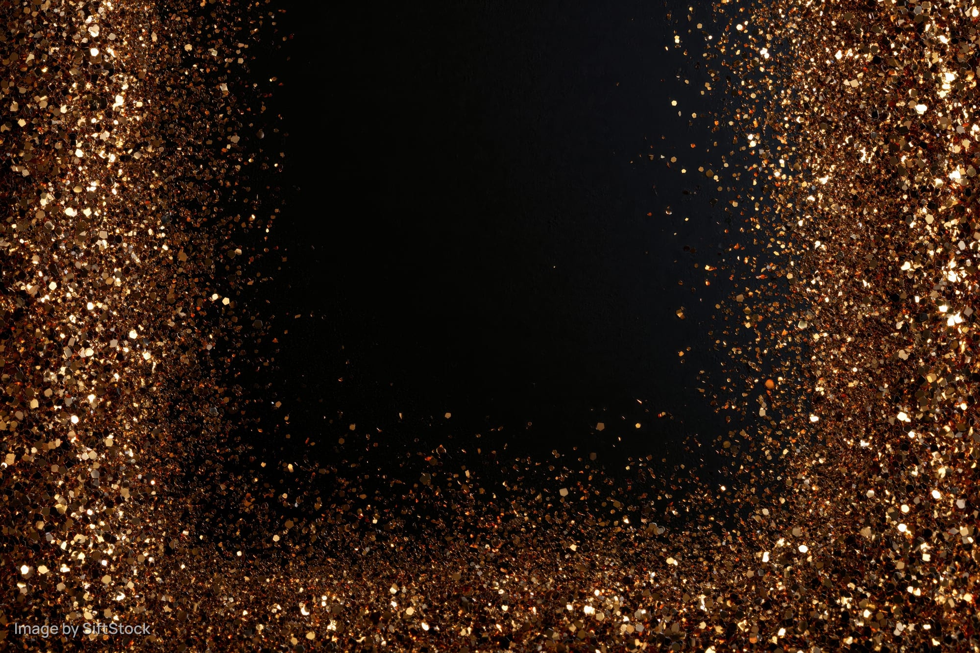 Gold glitter particles forming a sparkling frame around a dark center with copyspace